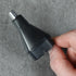 Hand holding a nose and ear hair trimmer attachment on a gray concrete surface