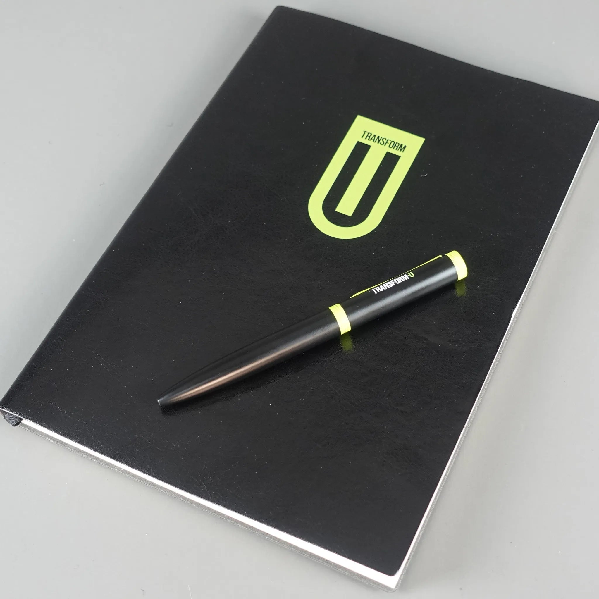 Black notebook with a logo and a pen on a gray background