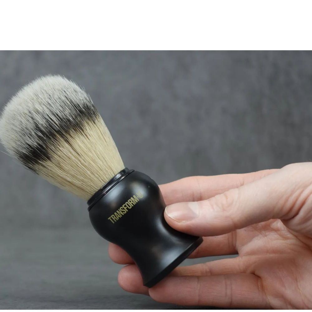 Hand holding a black shaving brush with gray bristles against a gray background