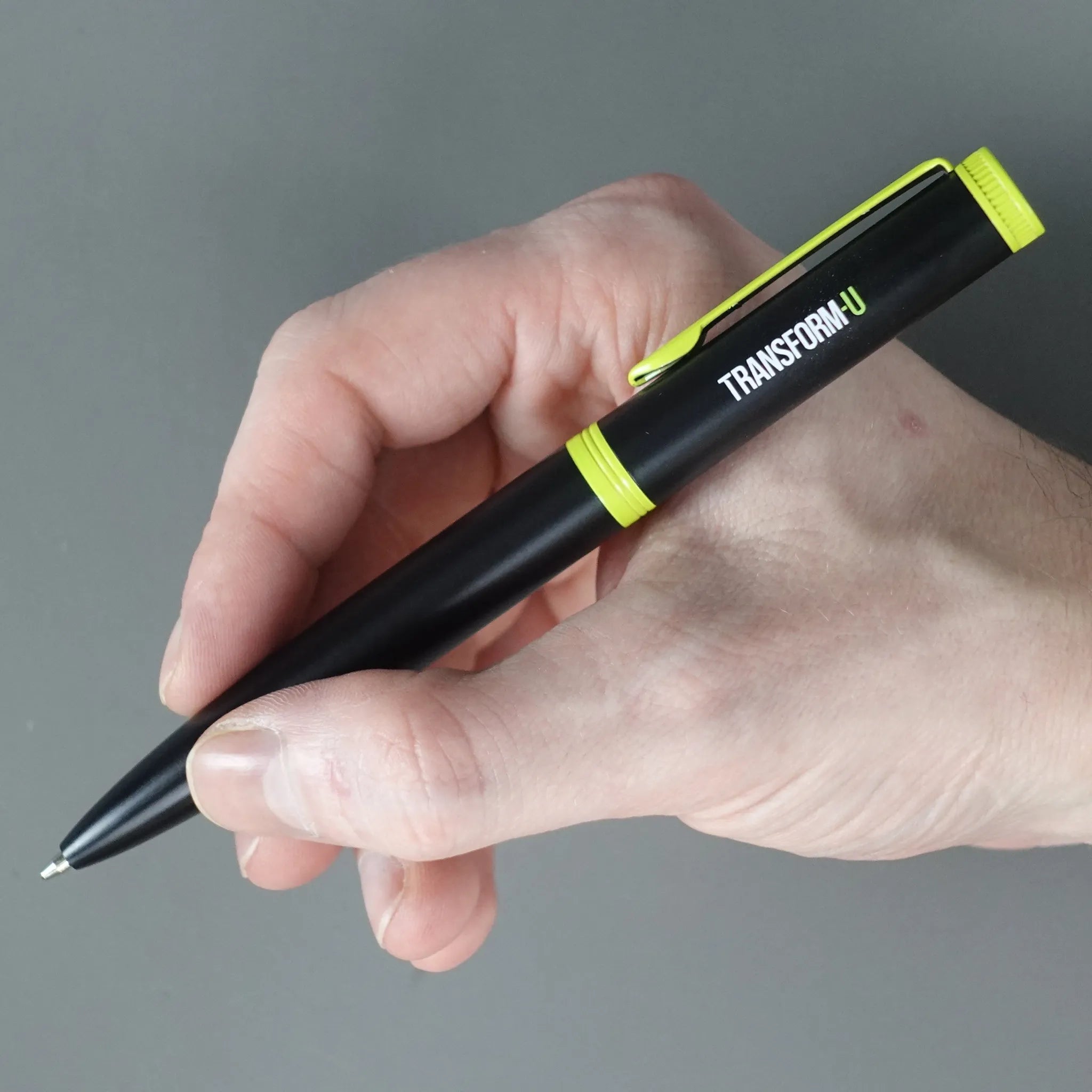 Hand holding a black pen with green accents on a gray background