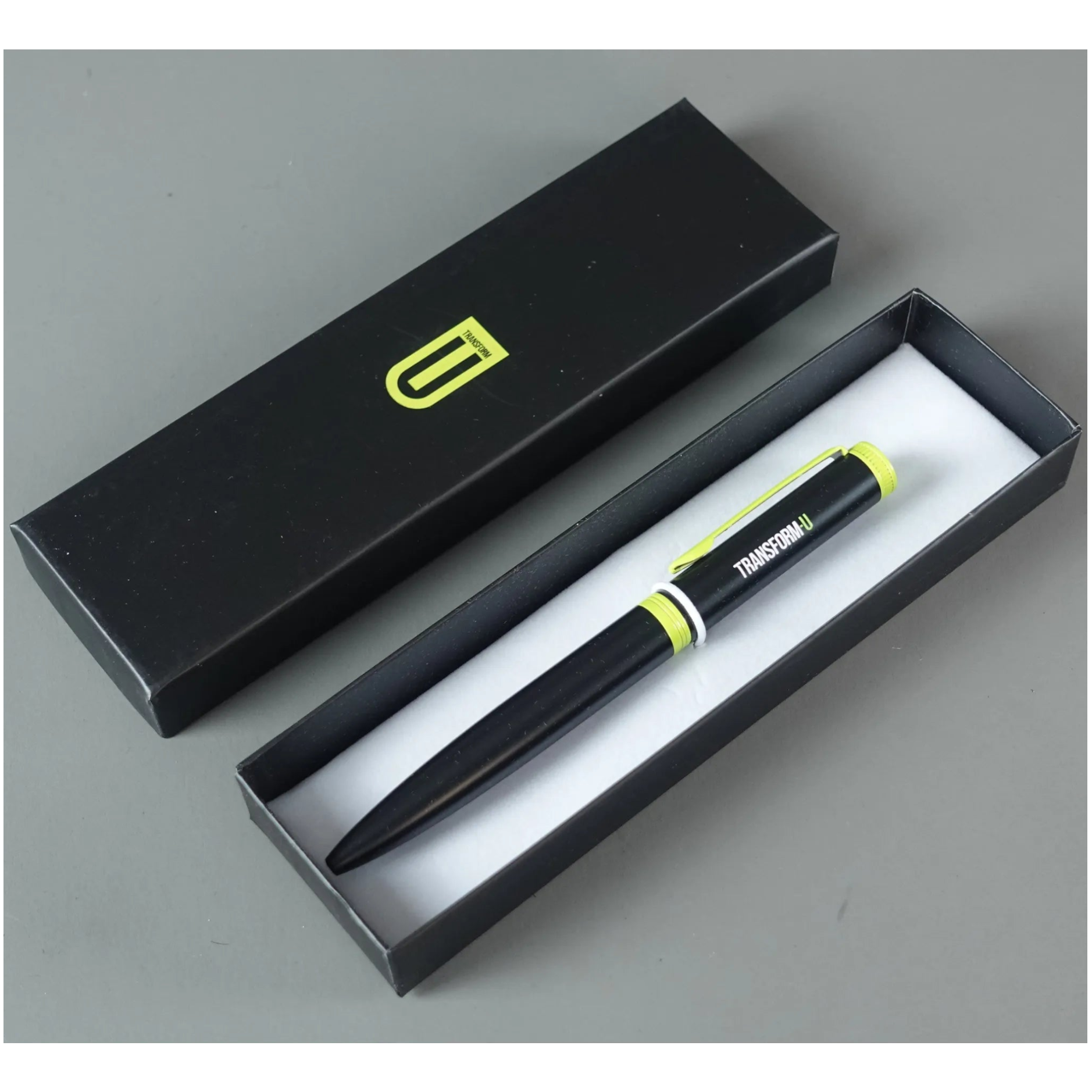 Black pen with green accents in an open black box on a gray background