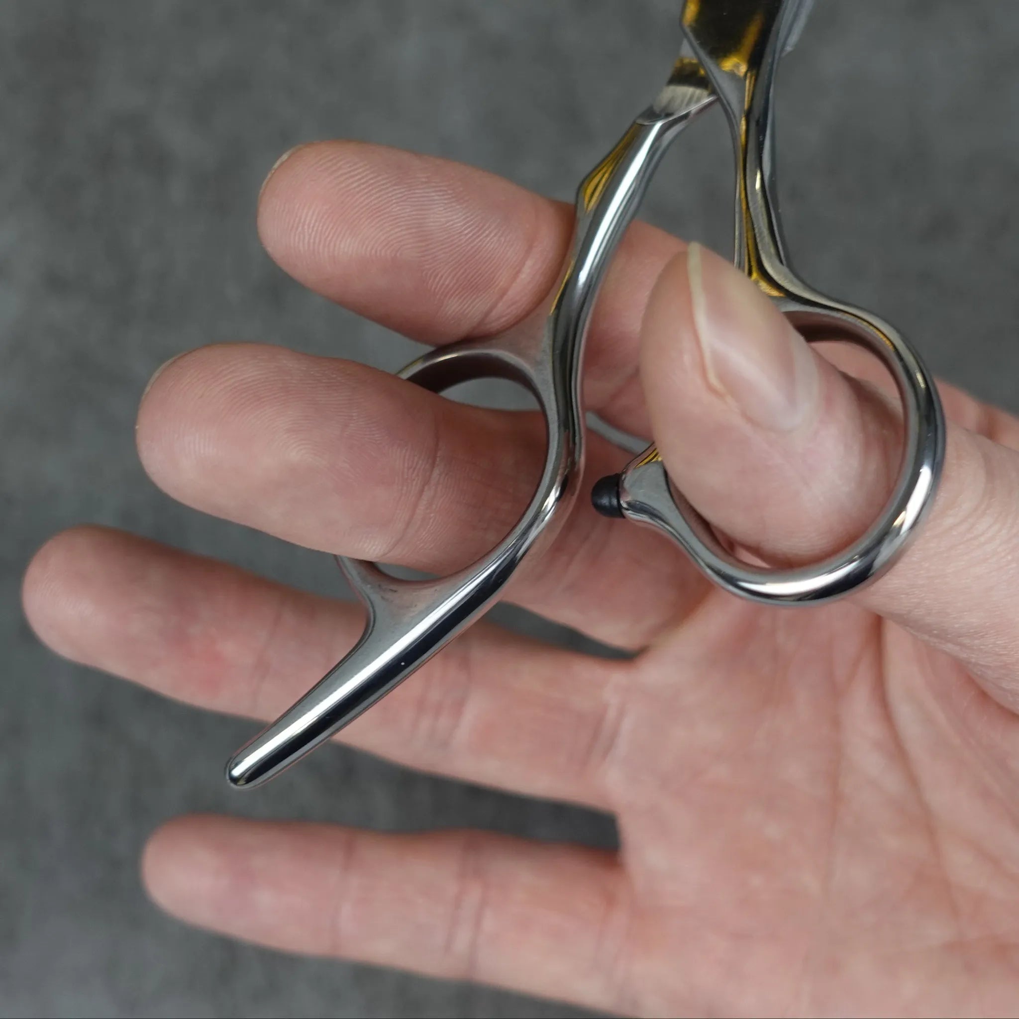 Hand holding a pair of silver scissors against a gray background