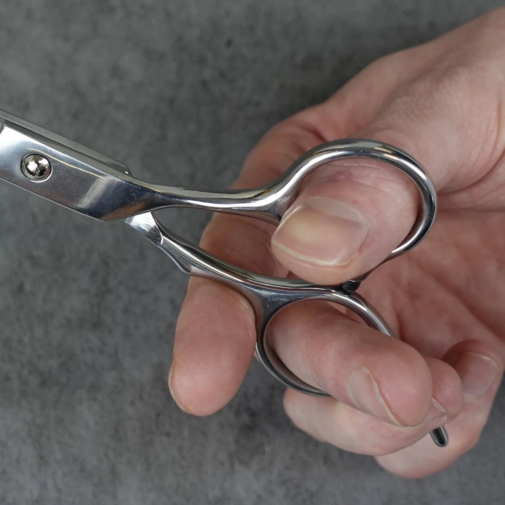 Hand holding a pair of silver scissors against a gray background