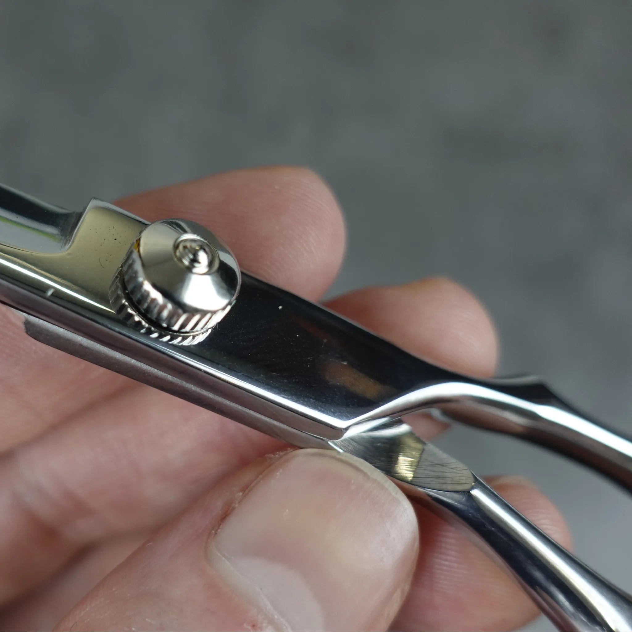 Close-up of a hand holding a pair of silver scissors against a blurred gray background