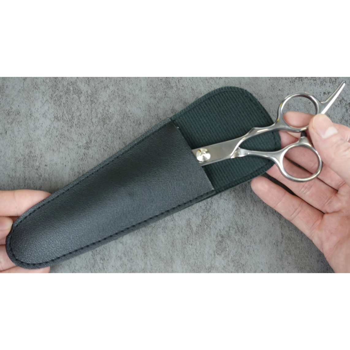 Scissors in a black sheath held by hands against a gray background