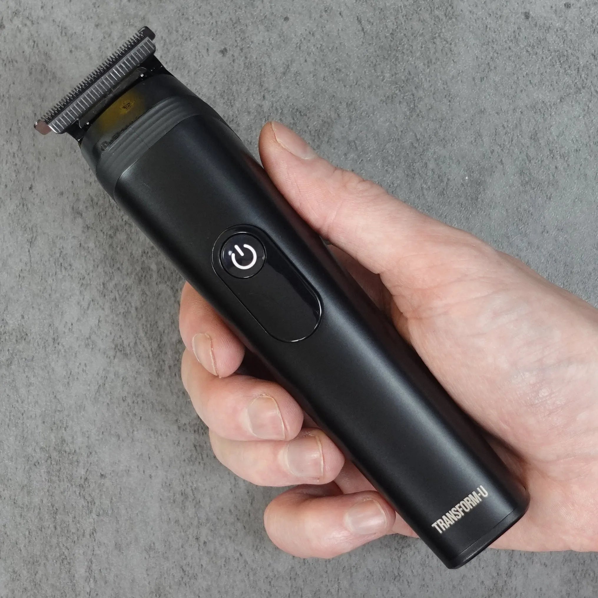 Hand holding a black hair trimmer against a gray background