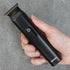 Hand holding a black hair trimmer against a gray background