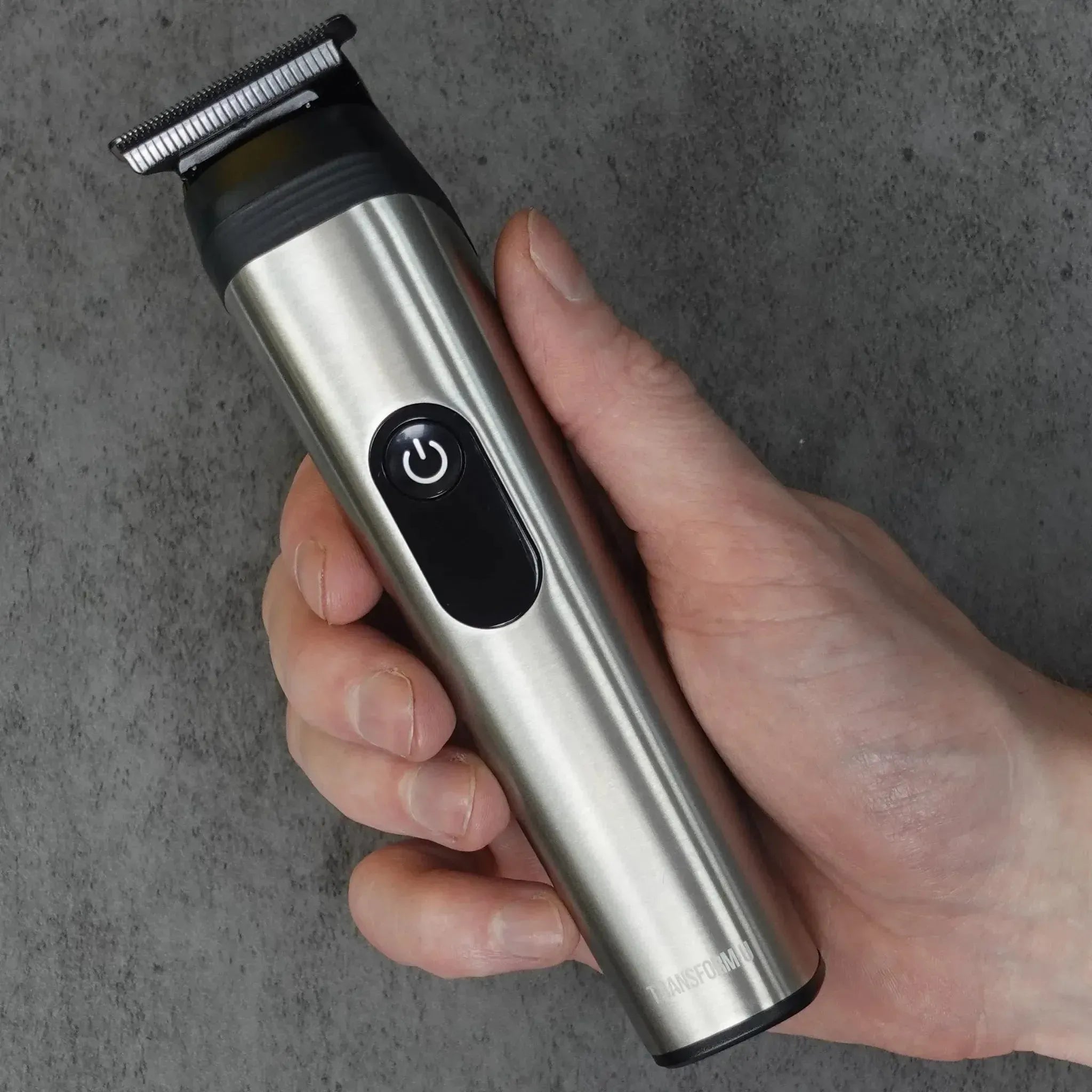 Hand holding a silver and black hair trimmer against a gray background
