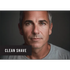Man with a clean-shaven face and gray hair, wearing a gray shirt against a dark background.