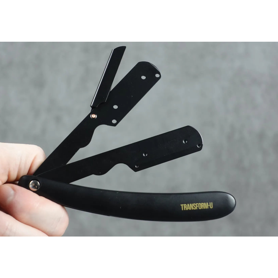 Black straight razor with 'Transform-U' branding held by a hand against a gray background