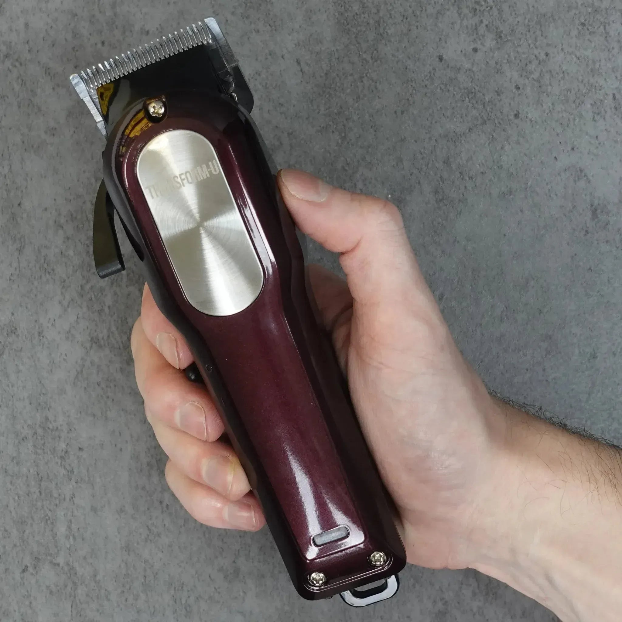Hand holding a maroon hair clipper against a gray background