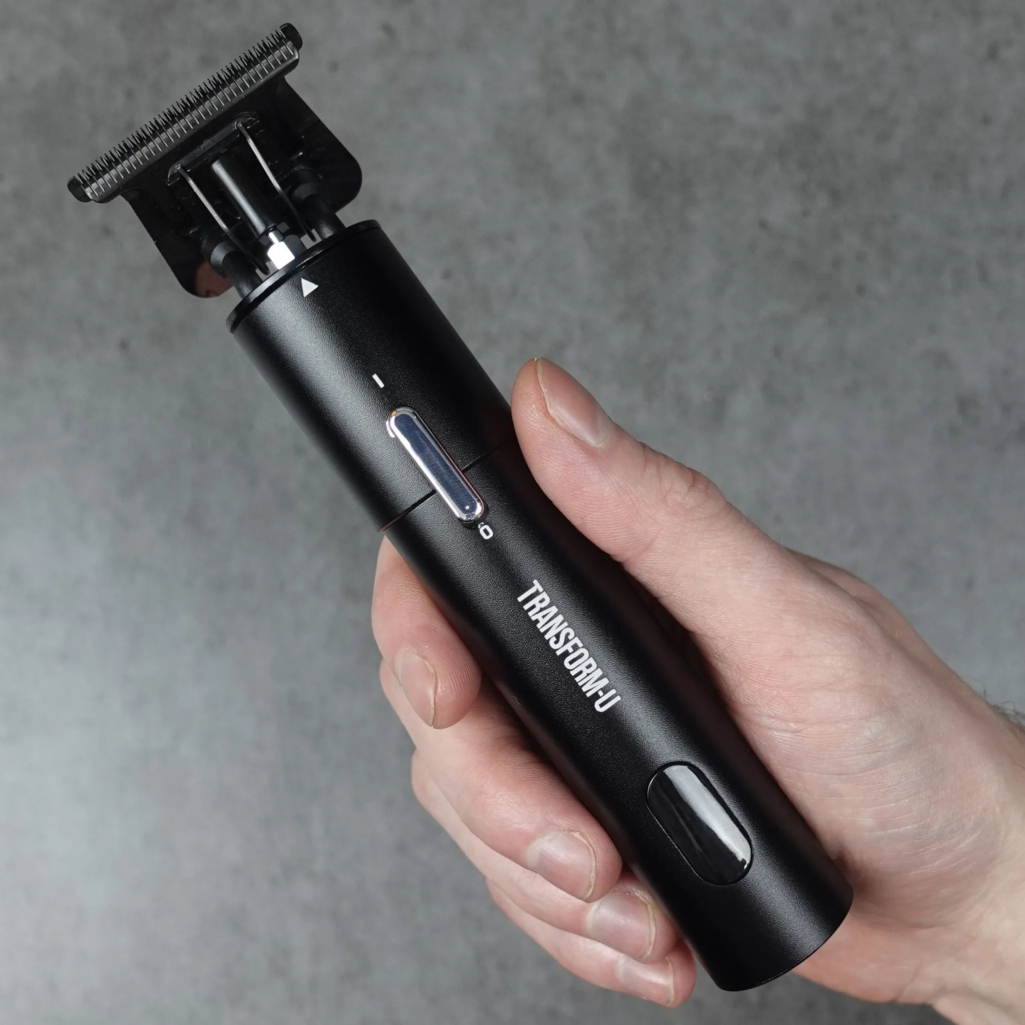 Hand holding a black hair trimming tool against a gray background