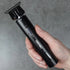 Hand holding a black hair trimming tool against a gray background