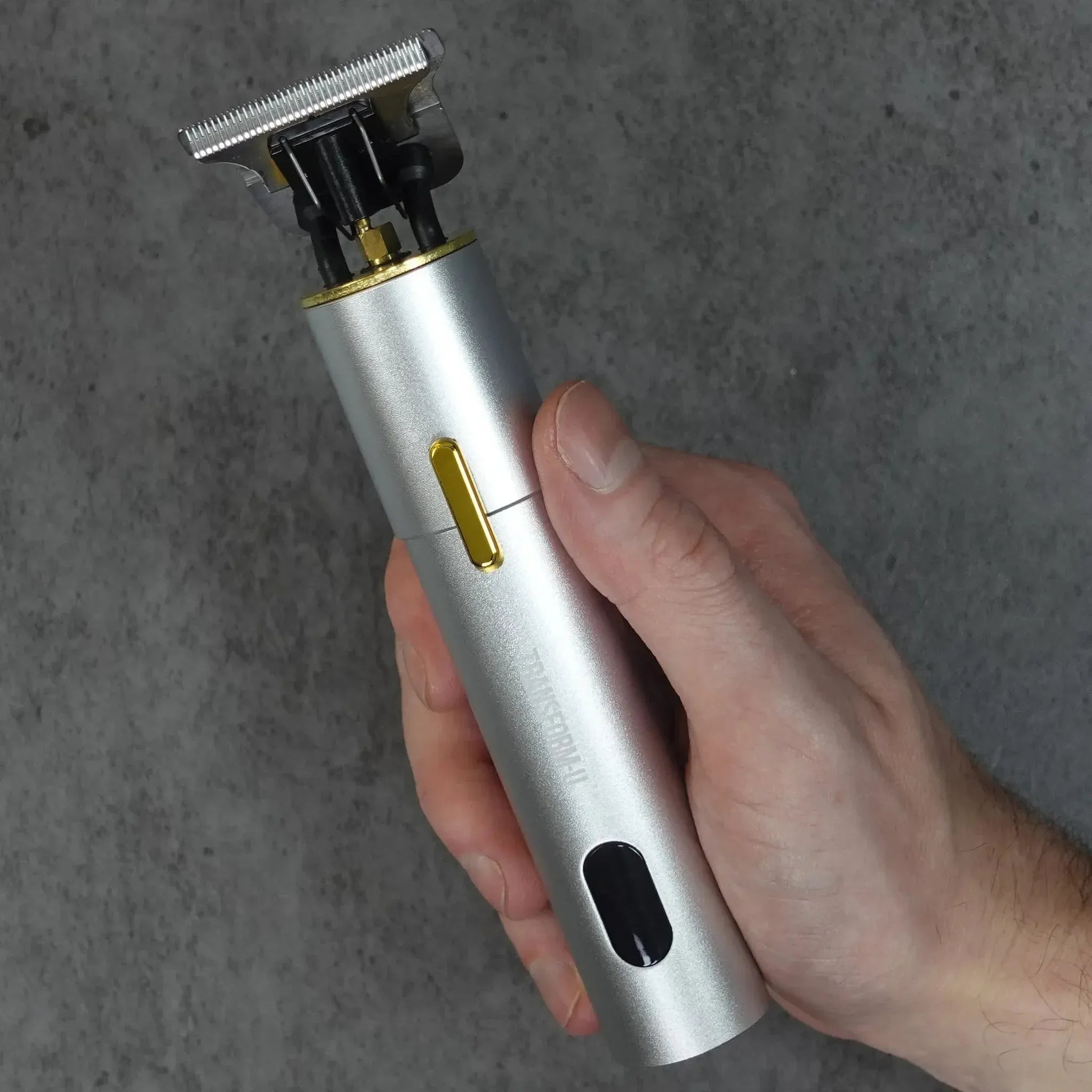 Hand holding a silver hair trimmer against a gray background