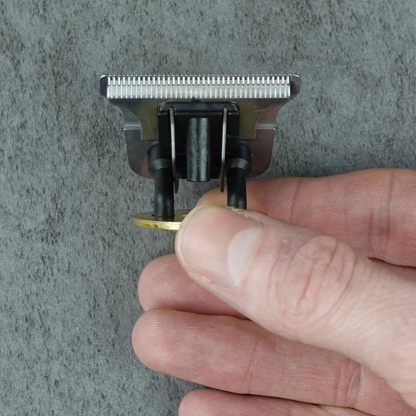 Close-up of a hand holding a small hair trimmer head against a gray background