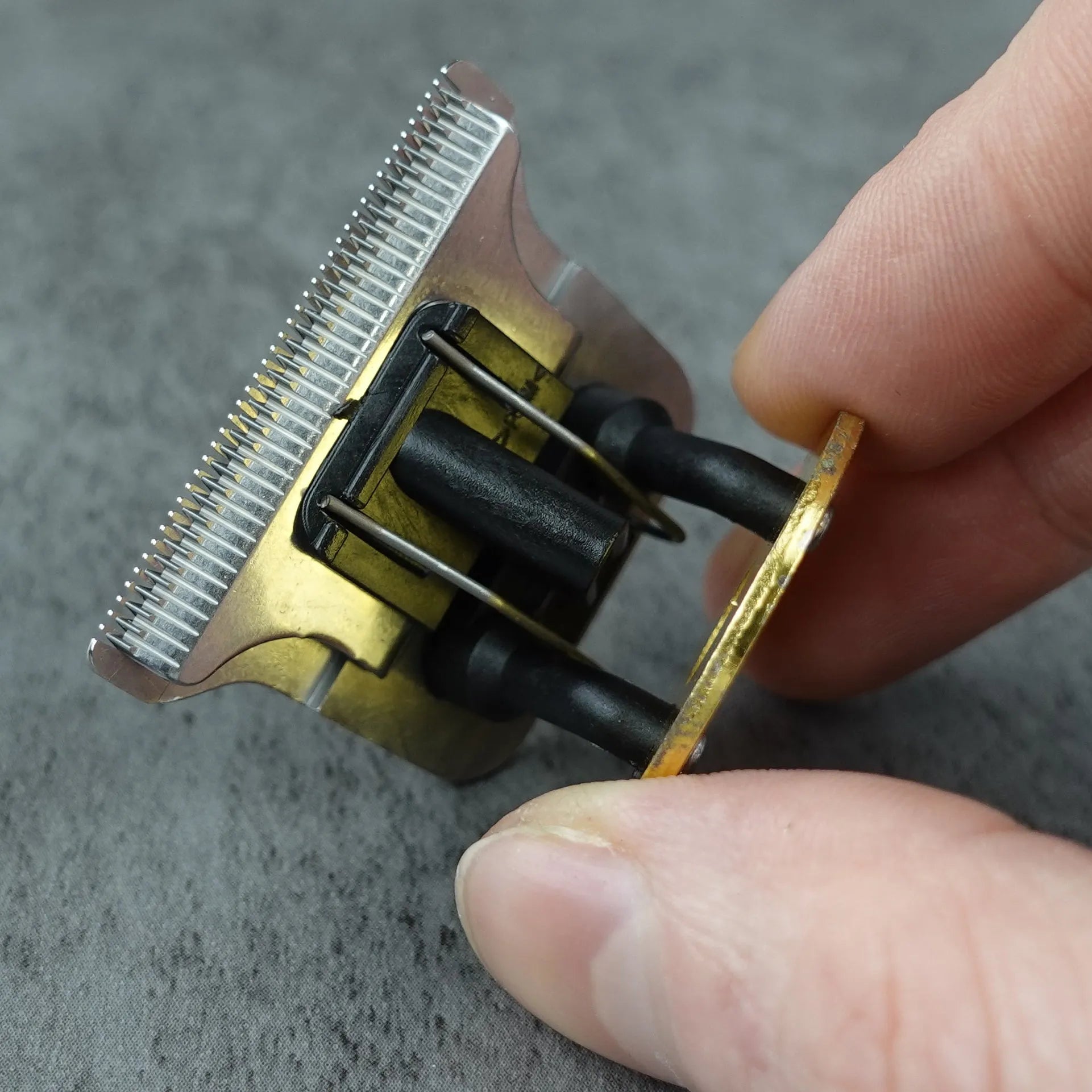 Hand holding a small hair trimmer head on a gray surface