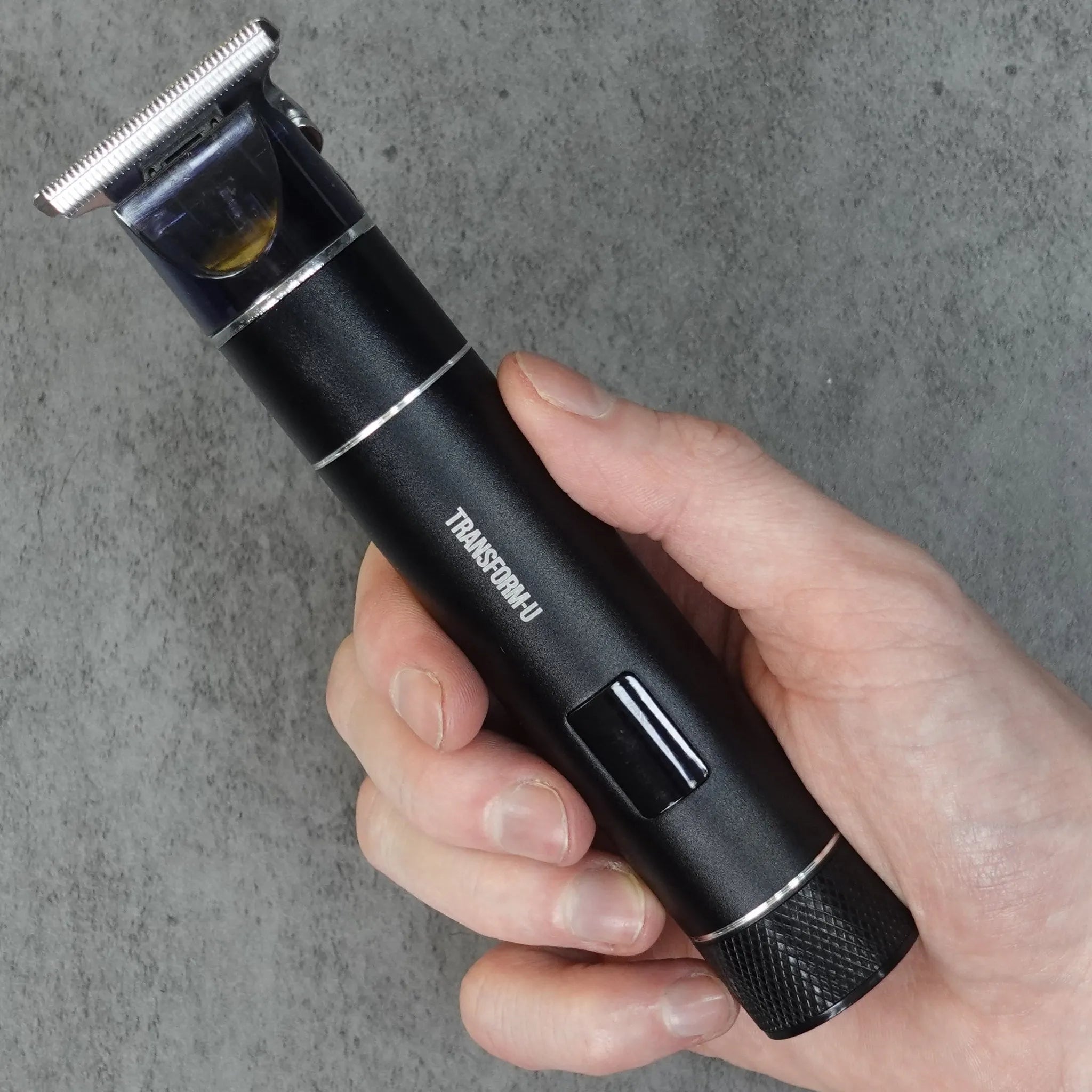 Hand holding a black hair trimmer with 'TRANSFORM-U' branding on a gray background