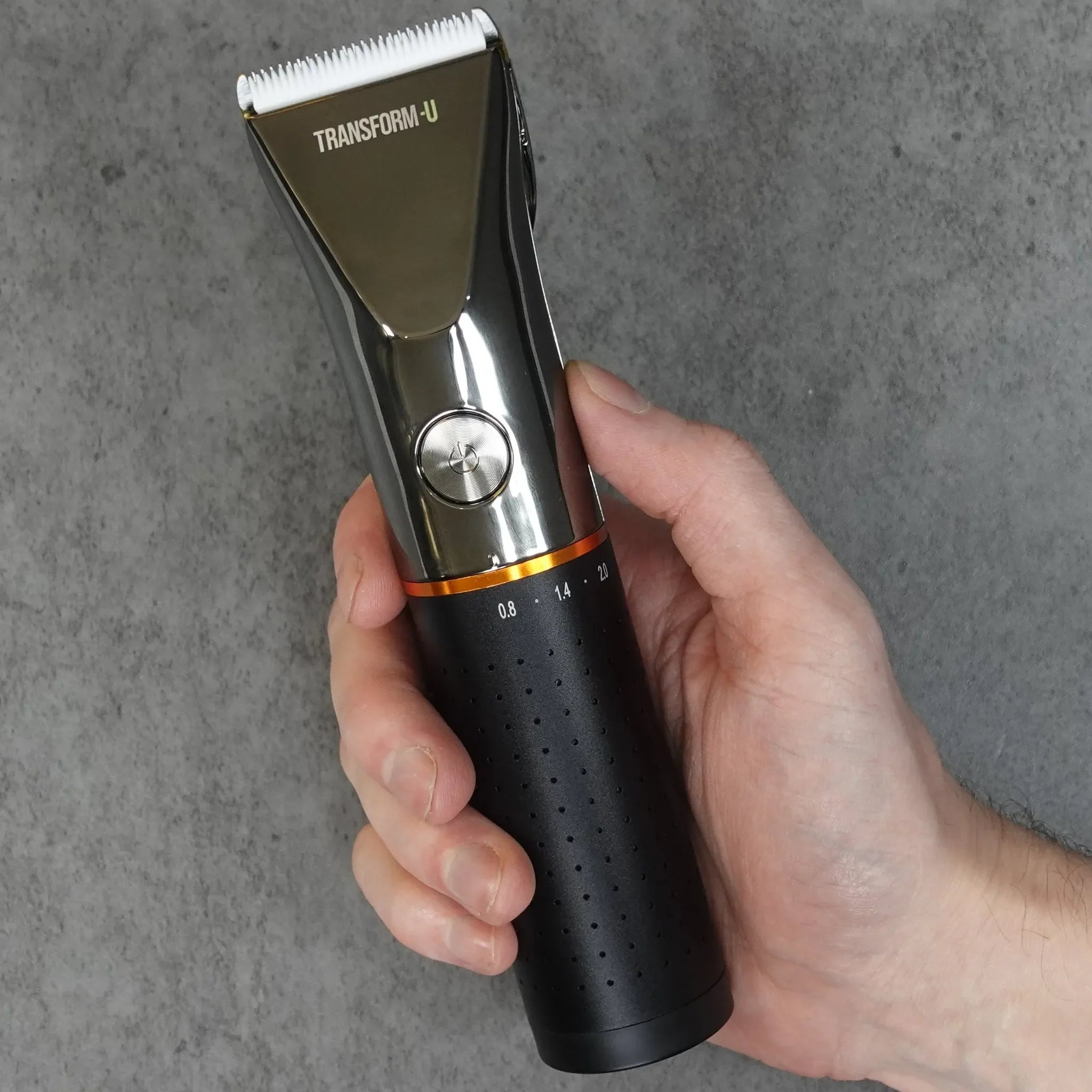 a black hair clipper being held by a hand against a grey background
