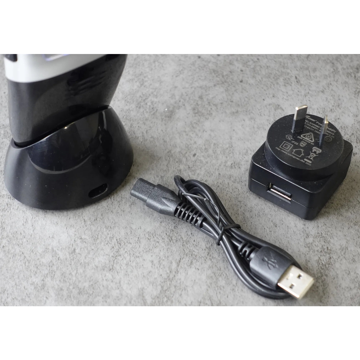 Black electrical travel shaver with charging cable and adapter on a gray surface