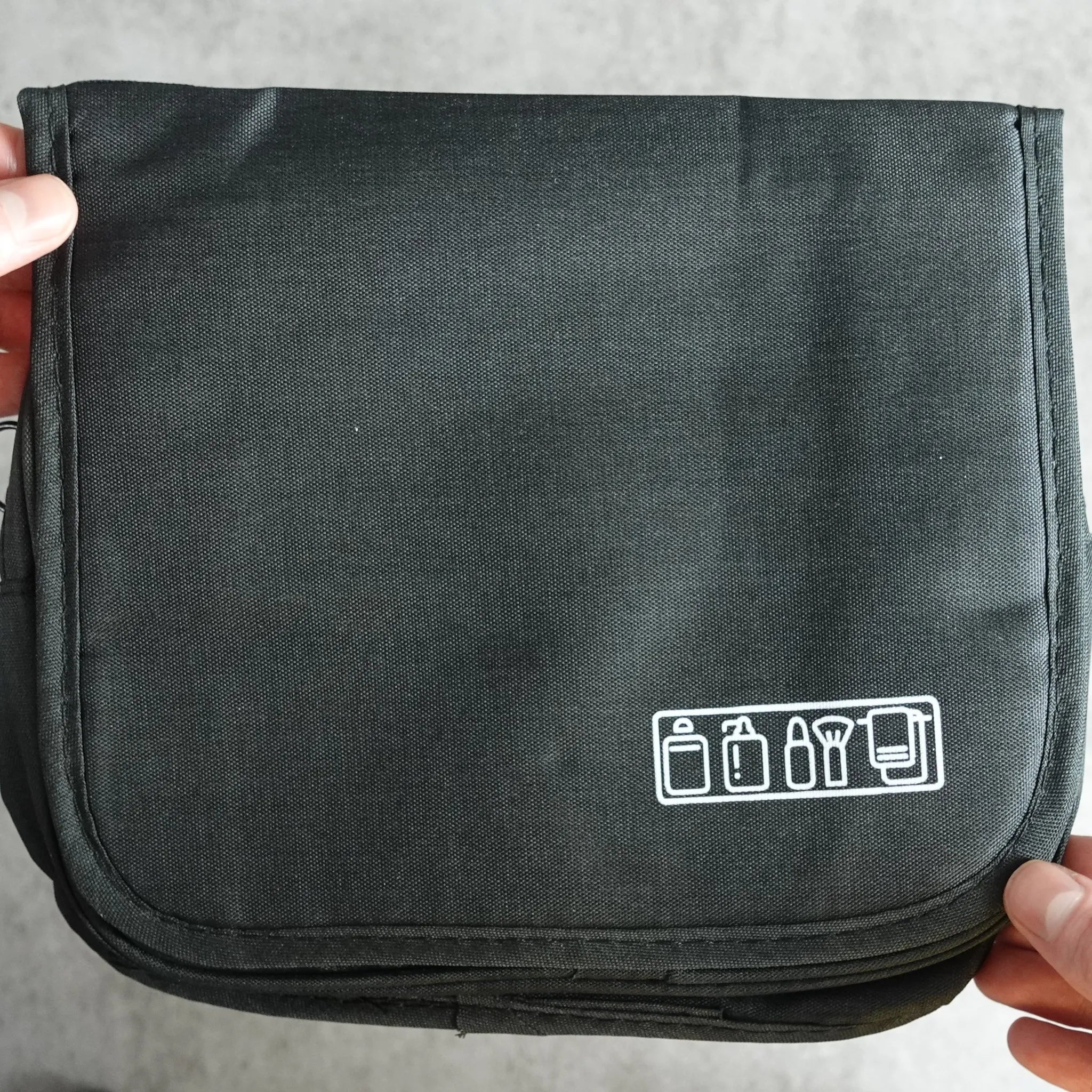Black toiletry bag held by hands on a light gray surface