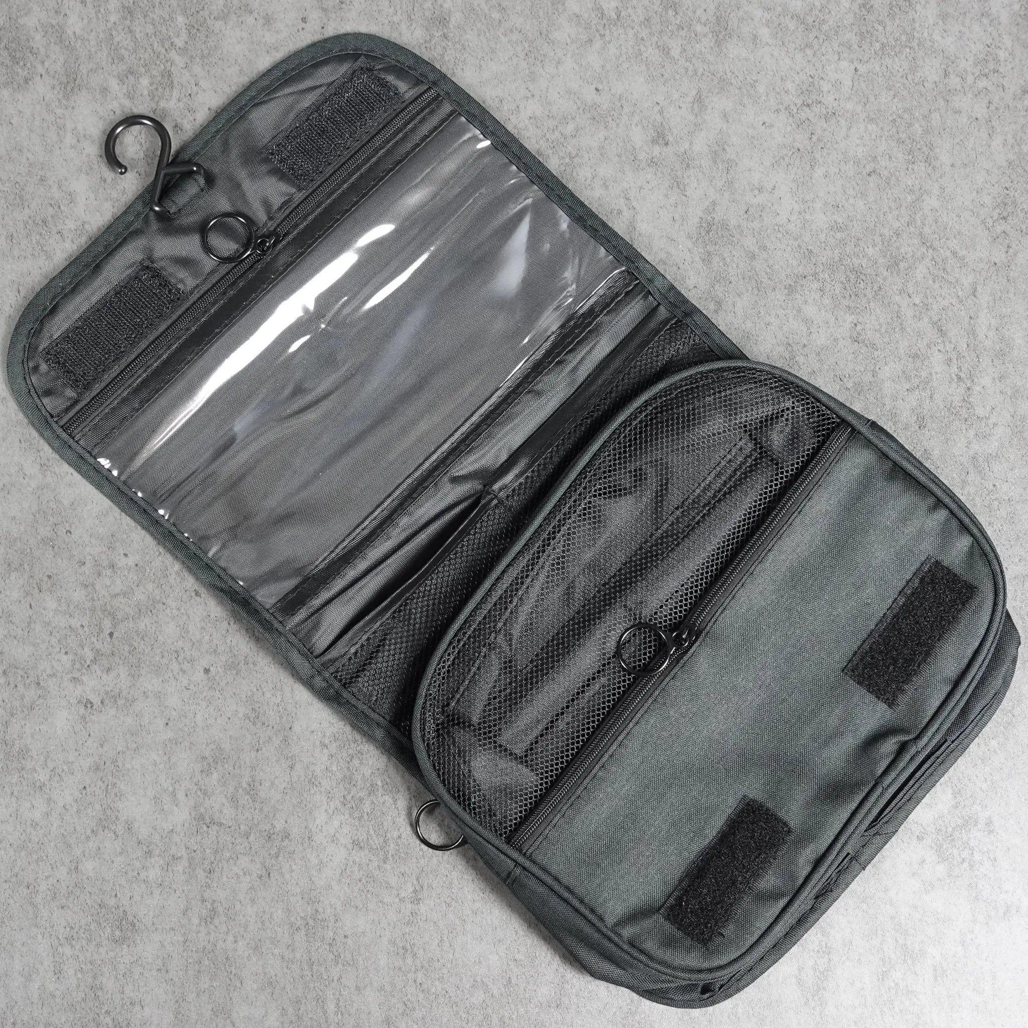 Black travel toiletry bag with clear compartments on a light gray surface