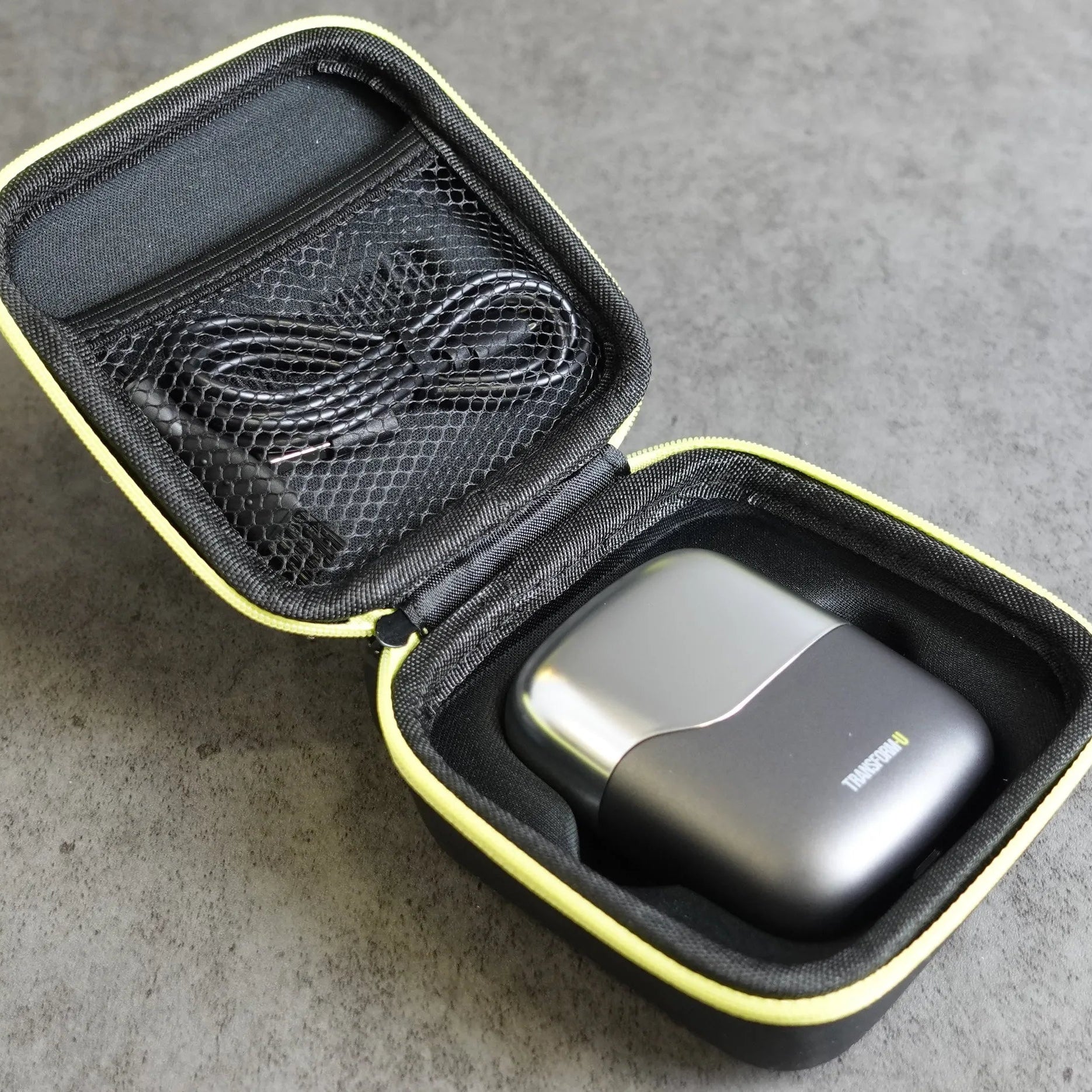 Black electric shaver in a carrying case with a cable on a gray surface