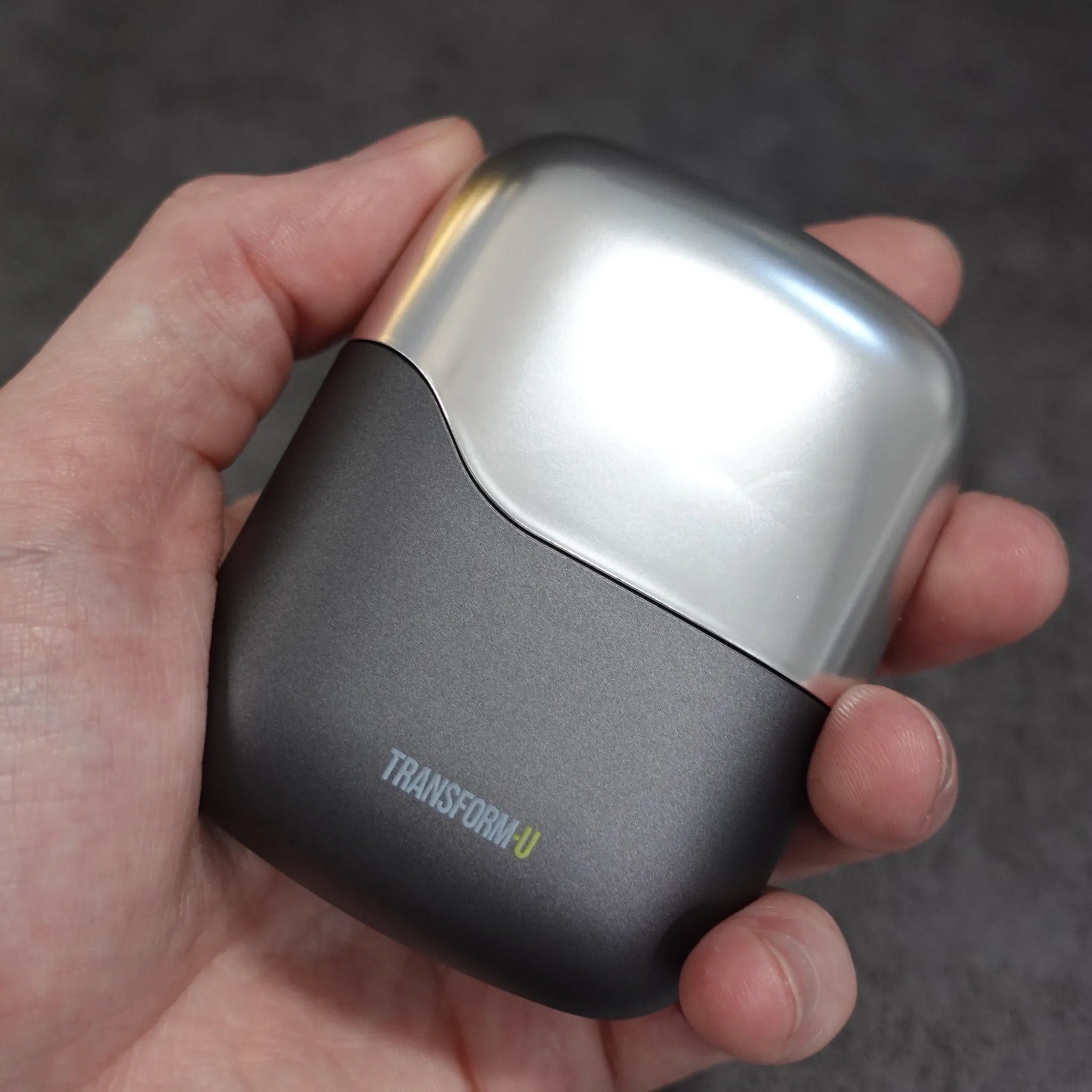 Hand holding a black and silver travel shaver with 'Transform-U' branding on a dark background