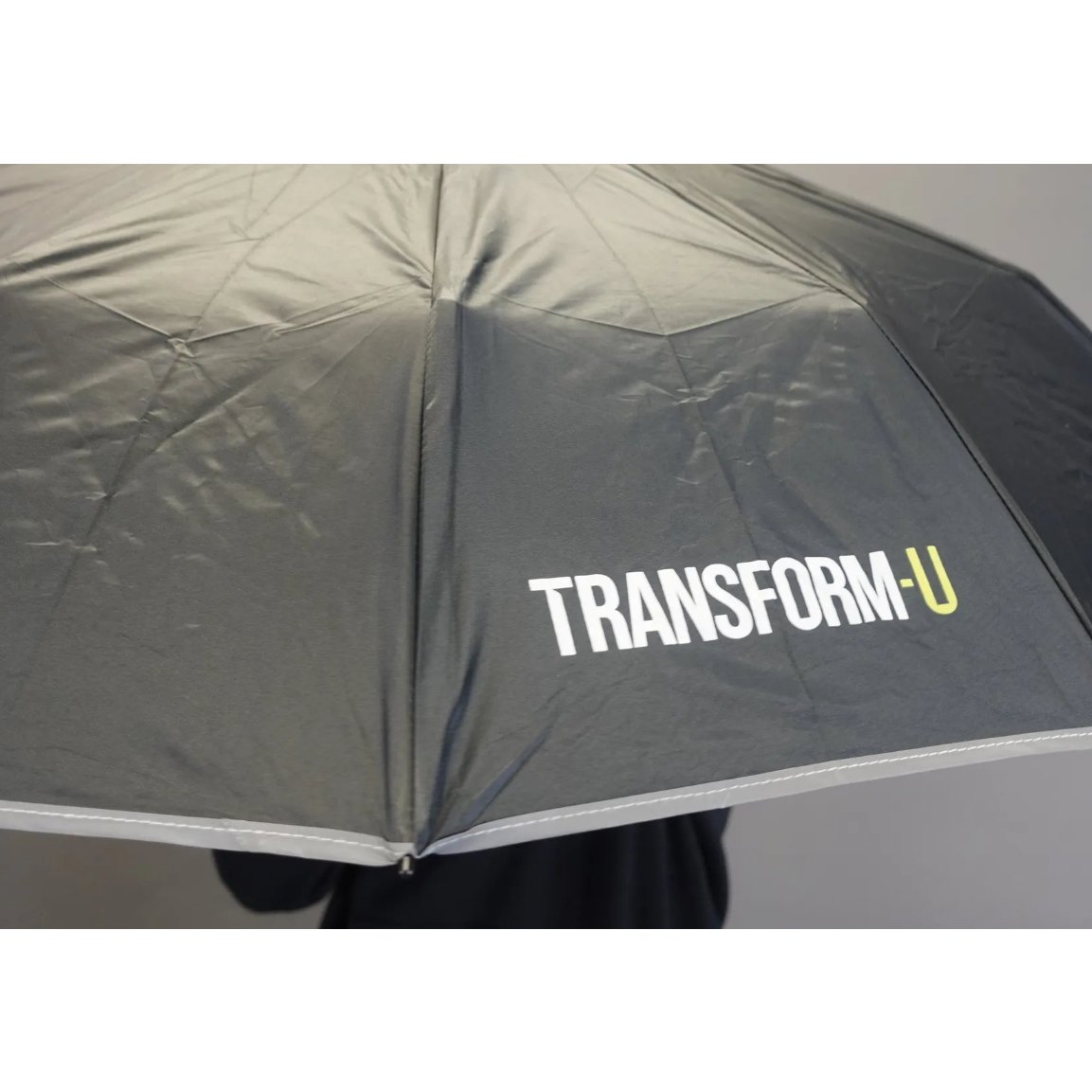 Black umbrella with 'TRANSFORM-U' branding on a gray background