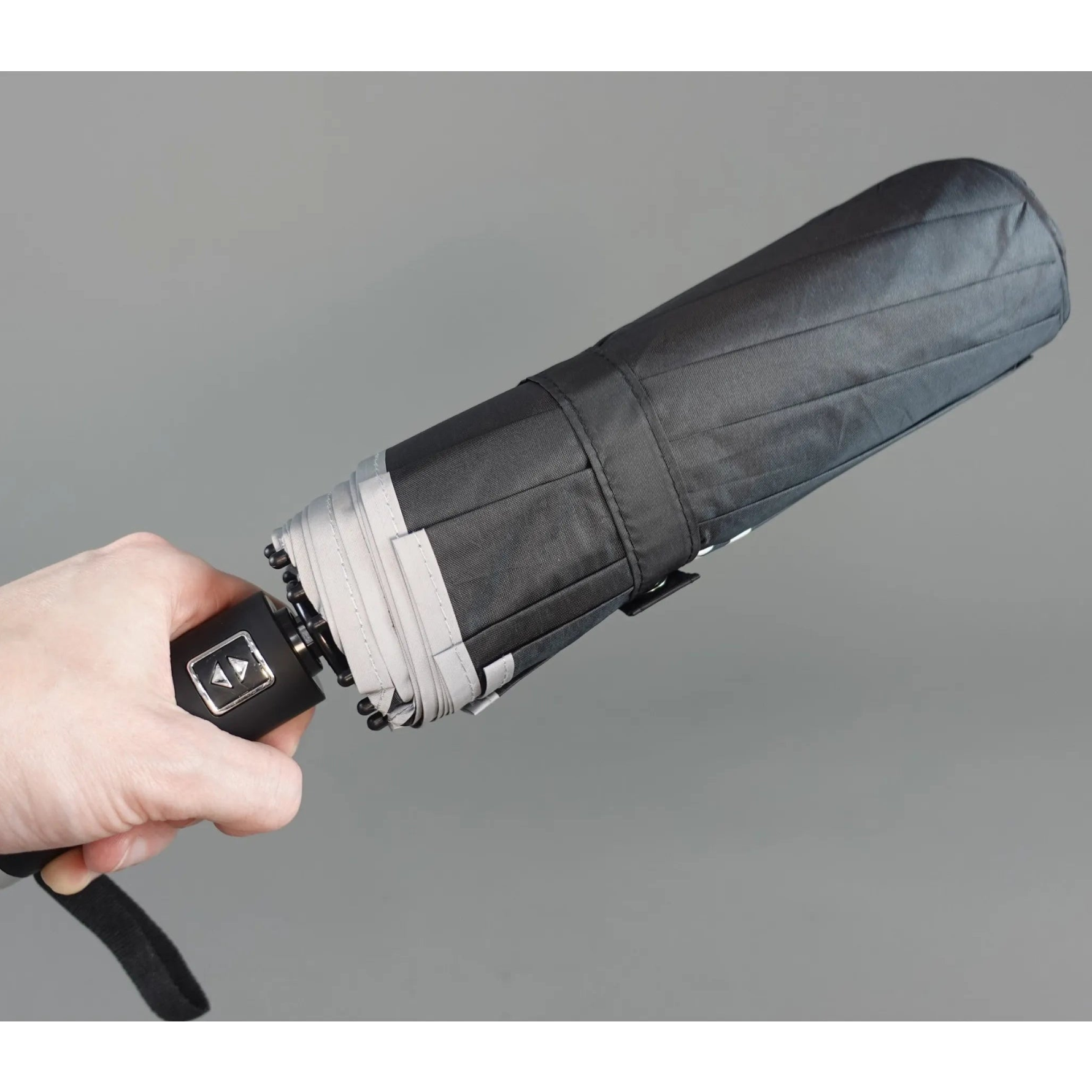 Hand holding a black umbrella against a gray background